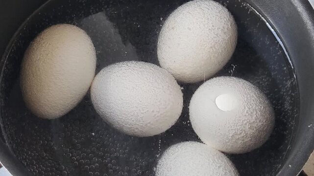 White chicken eggs are boiling in a black pot in the water.