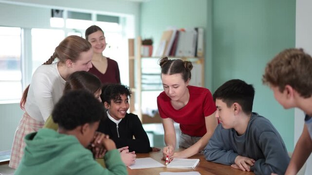 Focused multiethnic teens working on assignment at table under supervision of female instructor in classroom