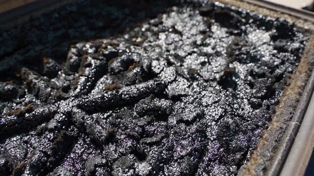 Heavy creosote and tar deposits on cast iron fireplace grate surface close up