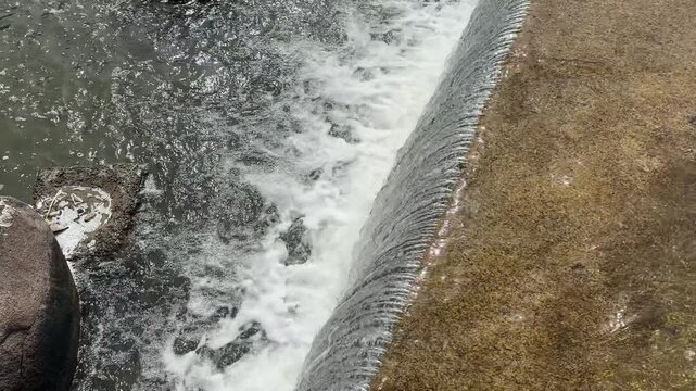 Flowing water over concrete spillway, abstract river cascade texture with white foam, fresh water movement and hydraulic overflow background.