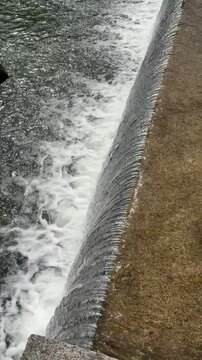 Flowing water over concrete spillway, abstract river cascade texture with white foam, fresh water movement and hydraulic overflow background.
