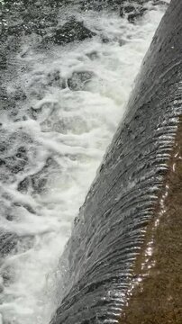 Flowing water over concrete spillway, abstract river cascade texture with white foam, fresh water movement and hydraulic overflow background.