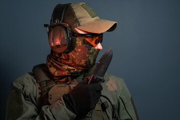 Studio profile portrait of a tactical military soldier in camouflage balaclava and active headphones holding a sharp combat knife in gloved hand © Dmitri