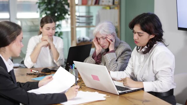 Group of women sitting at table looking tired and sad in office space