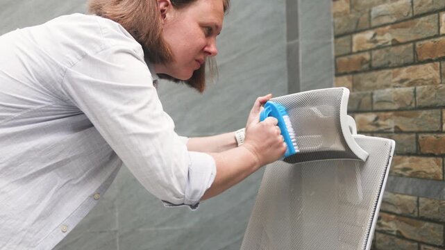 Deep cleaning chair fabric shows woman scrubbing mesh headrest. Modern easy-to-clean materials simplify deep cleaning chair fabric, as blue brush easily removes stains from durable mesh surface.