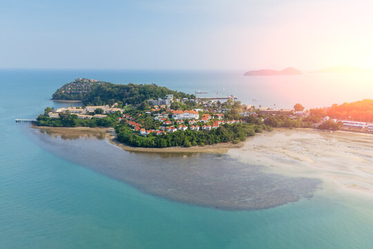 An expansive aerial panorama captures a vibrant coastal community, with numerous buildings nestled among green trees on a peninsula, bordered by blue ocean