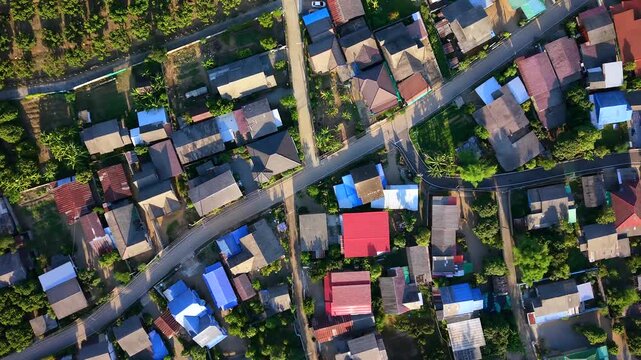 Vertical drone shot flying over residential suburban village with houses and colorful roofs Grid road street architecture with green gardens and trees during warm golden hour sunset light daytime