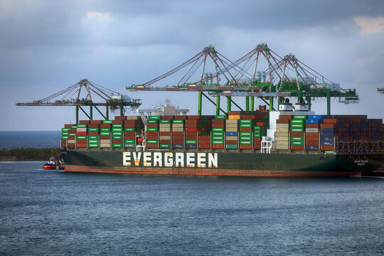 Large container ship fully loaded with freight cargo ocean transit. Industrial cargo vessel transporting global trade containers near port terminal terminal with cranes.