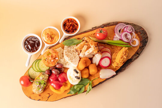 Top view of a traditional Romanian appetizer platter with pork fat, cheese, vegetables, and dips on a wooden board over a peach background.
