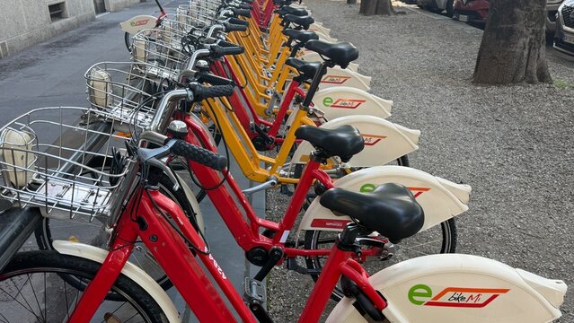 Rentable electric bicycles lined up neatly on a city street, ready for public use. Vibrant colors and modern design highlight sustainable urban transportation. Italy, Milan.