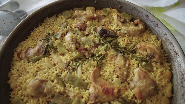 Close up detail of a traditional Spanish Valencian paella with chicken, rabbit and green beans in a pan on a table, frontal tracking shot moving backward.