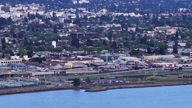 Expansive aerial perspective showing the cityscape of Albany and Berkeley, California, with the bay waters in the foreground and traffic moving along the coastal highway infrastructure