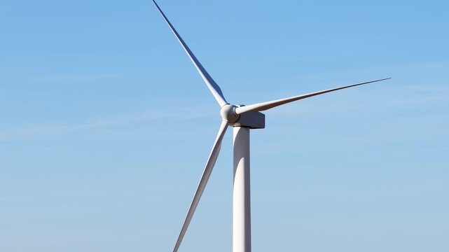 Close-up of a wind turbine spinning its blades against a clear blue sky, generating clean, renewable, and sustainable electricity for a green future at the Altamont Pass wind farm