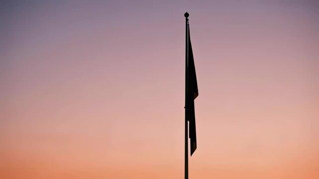 Fluttering dark flag on metal pole responding to light breeze at dusk, halyard visible against sky