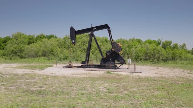 Drone 4K of a field with an oil pump jack in the spring and summer.