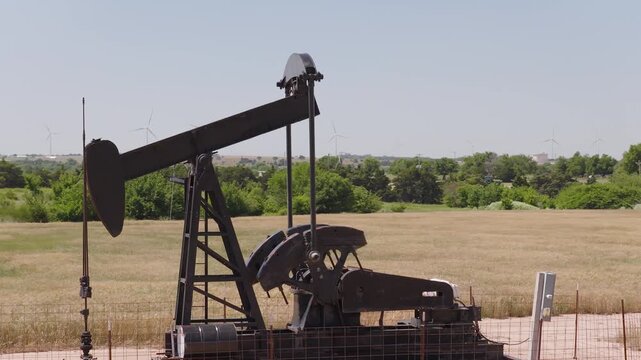 Drone 4K of a wheat field with two oil pump jacks and wind turbines in the background.