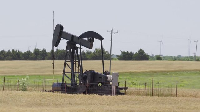 Drone 4K of a wheat field with two oil pump jacks and wind turbines in the background.