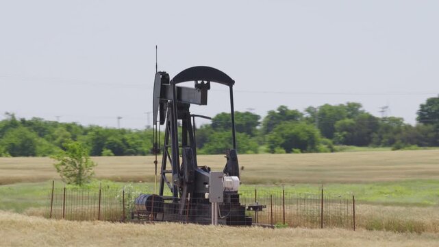 Drone 4K of a wheat field with two oil pump jacks and wind turbines in the background.
