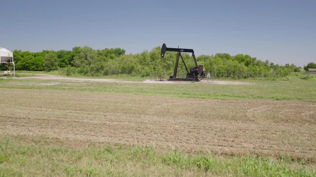 Drone 4K of a field of hay bails surrounding an oil pump jack in the spring and summer.