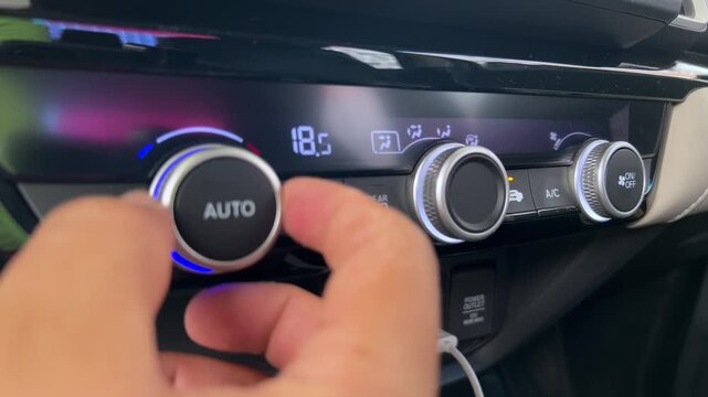 Close view of hand adjusting digital climate control temperature settings on modern vehicle dashboard with illuminated automotive controls and display