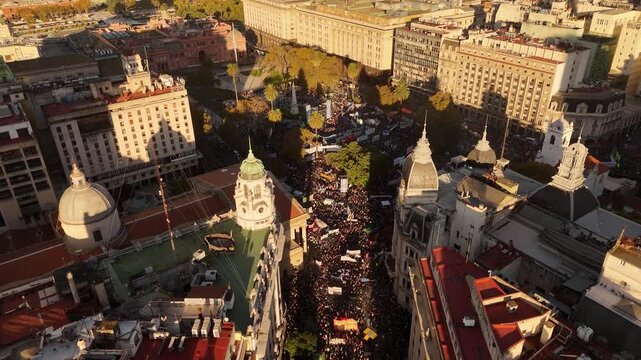 Drone view of protesters marching through city streets to join massive demonstration in Plaza de Mayo at sunset in Buenos Aires, Argentina. Aerial forward