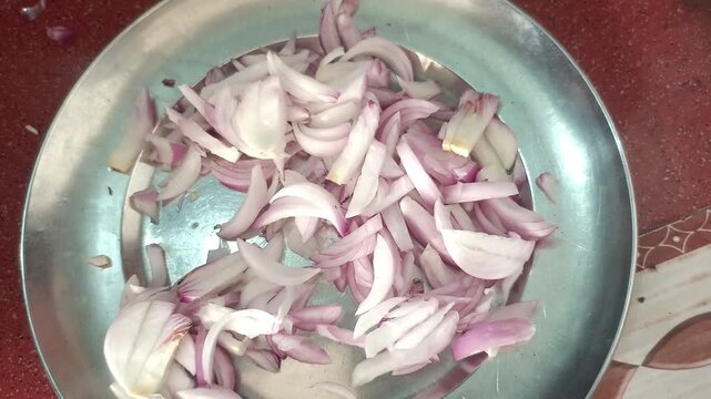 Top view of putting a whole red onion next to sliced onion pieces in a steel plate, food preparation