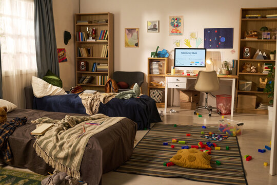 Wide shot of messy kids bedroom showing study desk with desktop computer, books, toys, beds. Suitable for education, child development, home organization, parenting content