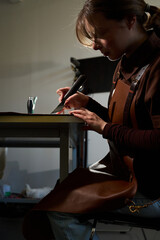 Fototapeta premium Female artisan cutting raw natural leather around a paper pattern in a workshop.
