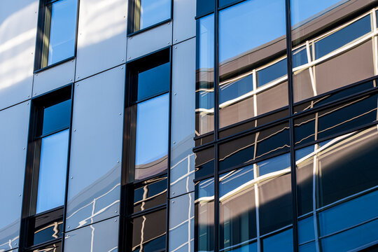 Blue reflection breaks across a glass building facade as windows and shadow shape urban office architecture with angular geometric detail