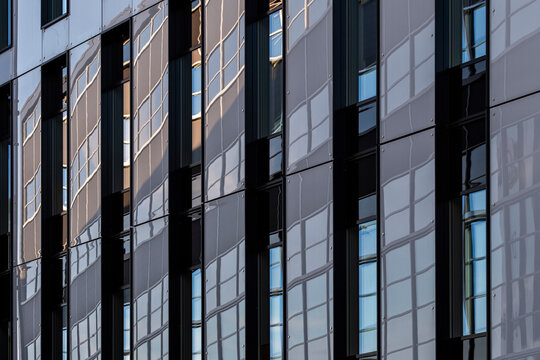 Dark vertical rhythm defines a glass building facade where windows and reflection give urban office architecture layered depth and narrow detail