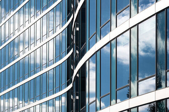 Curved glass windows sweep across a building facade where reflection and sky give urban office architecture a clean abstract pattern