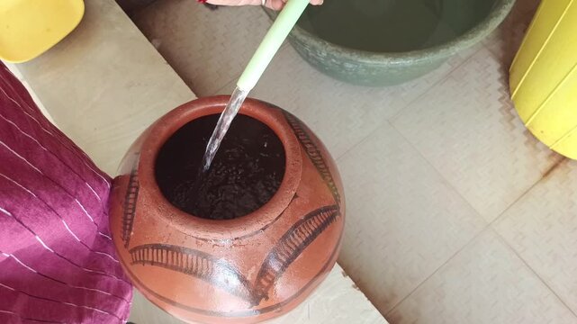 Filling fresh drinking water in a traditional Indian clay pot or matka with a pipe