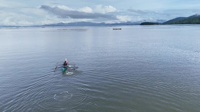 Aerial view of a traditional outrigger boat traversing tranquil waters during a calm summer morning.