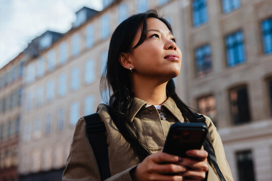 Young woman with phone looking up in city
