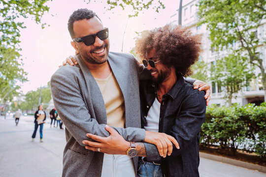 Two latin american friends with sunglasses, embracing outdoors, laughing and enjoying their time together at city.