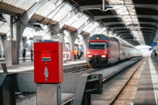 Paper ticket validation machine located inside the Zurich Main Station (Z&uuml;rich HB) in Switzerland, with local trains approaching at platform's entrance, modern Swiss railway public transportation
