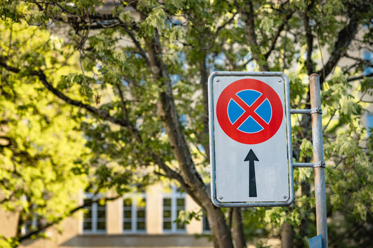 Standard European "No Stopping" restriction traffic sign (clearway sign or Halteverbot), located in Zurich city, Switzerland, prohibited parking for car vehicles next to local park with Summer trees