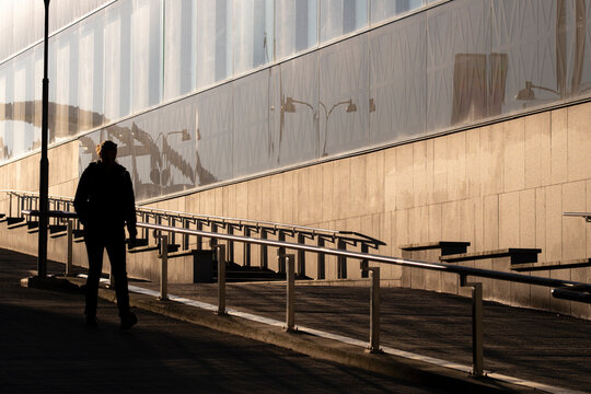 A silhouette on a quiet walkway near railing and stairs, as sunlight throws long shadows across an urban building facade and architecture