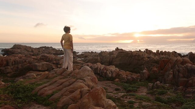 young boy exploring rocky coastline of DeKelders, Gansbaai, South Africa at sunset