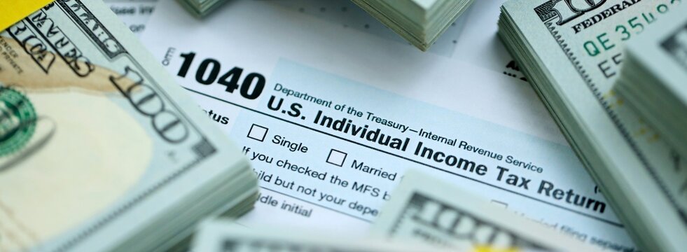 1040 Individual Income tax return form and hundred dollars money bills packs on accountants table