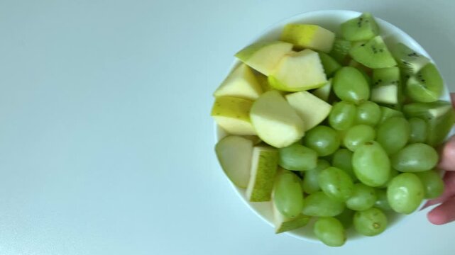 A woman puts a plate of sliced fresh fruits on the table. Diet, weight loss, low-calorie diet, vitamins. Taking care of your figure, striving for a healthy lifestyle and weight control