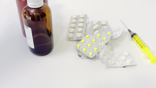 Medical professional preparing medication treatment with pills, syrup, saline solution, and a syringe on a sterile white background in a hospital or laboratory setting