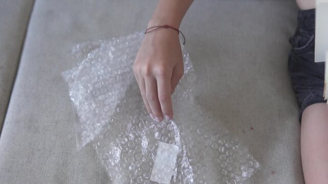 Close up of a childs hand popping bubble wrap on a soft fabric surface