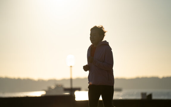 Senior woman jogging at sunrise by the harbour, active healthy lifestyle concept