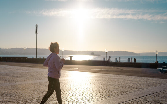Senior woman jogging at sunrise by the harbour, active healthy lifestyle concept
