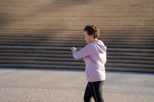 Senior Asian woman checking smartwatch while jogging outdoors, active healthy lifestyle concept