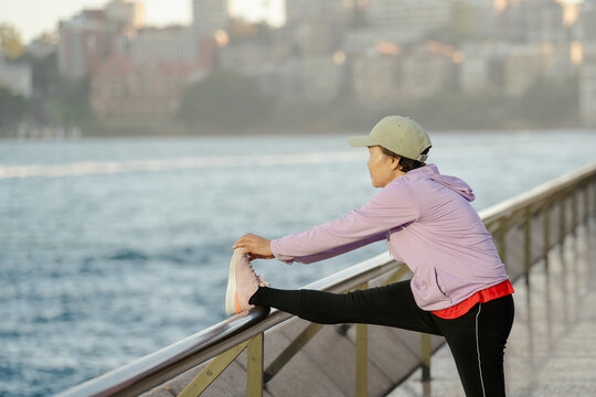 Senior Asian woman stretching leg on railing near Sydney Harbour Bridge at sunrise, Sydney, Australia. Apr 29,2026