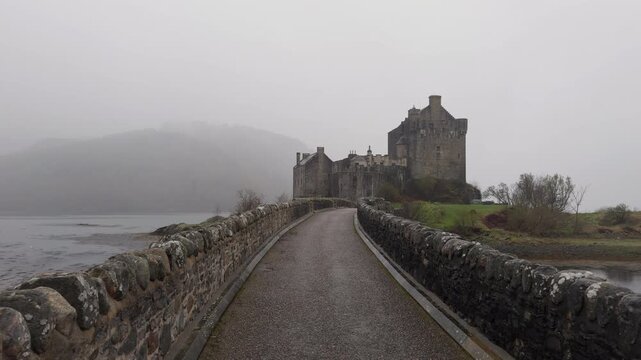 Eilean Donan Castle, Scotland. Panoramic walking shot across the bridge. Cloudy grey skies frame the medieval fortress. Cinematic Highland footage