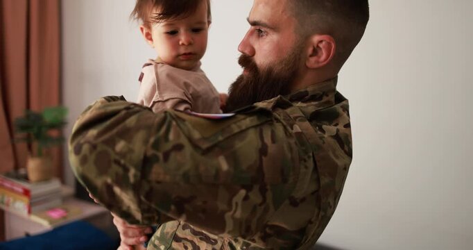 Male russian soldier in military uniform hugs his little son at home while baby boy touching russian flag - Emotional military happy homecoming concept 