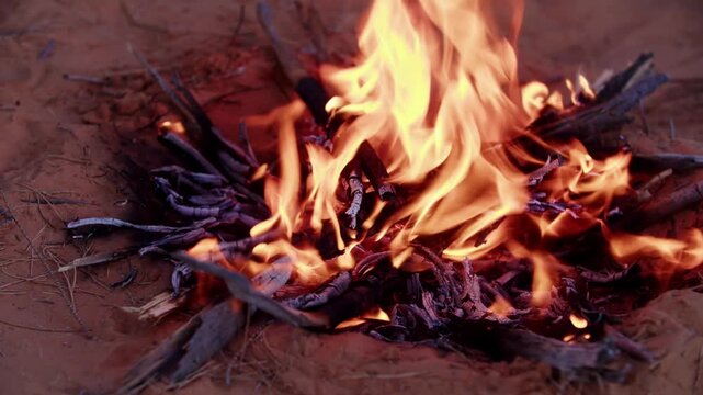 Close-up of a traditional campfire burning at sunset in the Tunisian Sahara Desert, creating a warm and authentic nomadic atmosphere under the evening sky